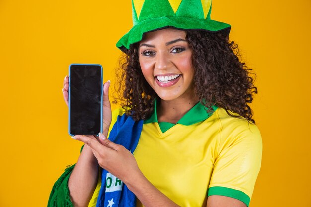 Brasilianischer fan, der ein smartphone mit kopienraum hält. brasilianische unterstützerin mit handy mit weißem bildschirm zum schreiben von text.