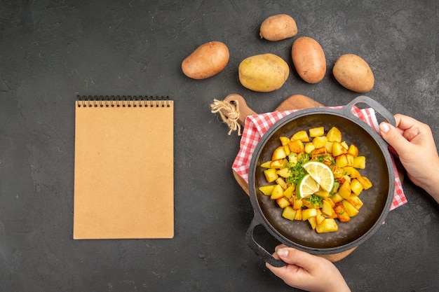 Bratkartoffeln von oben in der Pfanne mit frischen Kartoffeln auf dunkelgrauem Hintergrund