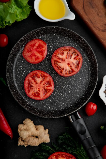Bratpfanne Tomaten mit Ingwer und Schüssel geschmolzene Butter auf schwarzem Tisch herum