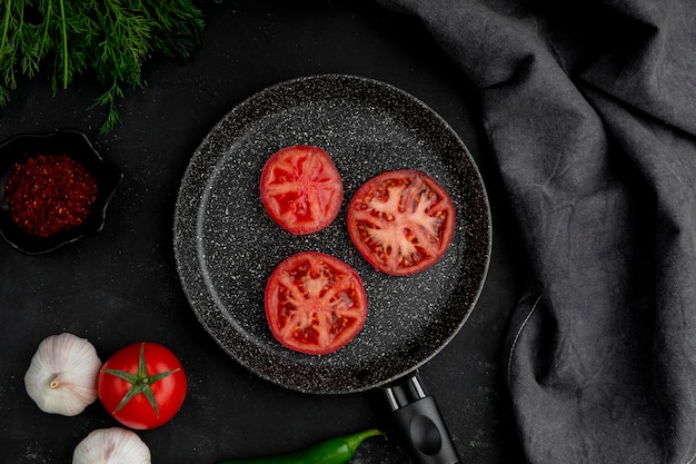 Bratpfanne Tomaten mit Knoblauchfenchel und Gewürzen auf schwarzem Tisch