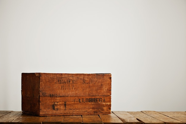 Braune getragene rustikale Schachtel mit schwarzen Buchstaben auf einem Holztisch in einem Studio mit weißen Wänden