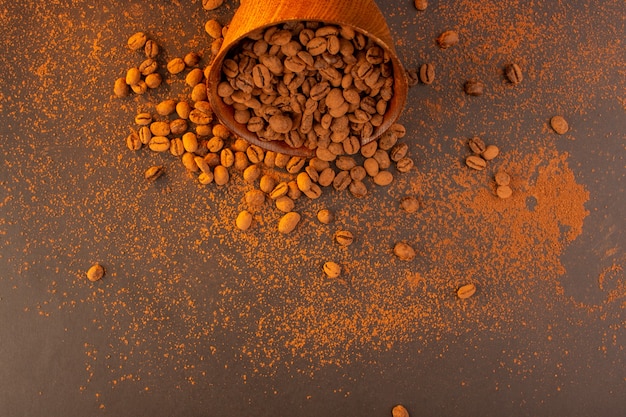 Braune Kaffeesamen der Draufsicht innerhalb der braunen Platte auf dem dunklen Körnchengranulat des braunen Hintergrundkaffeesamens