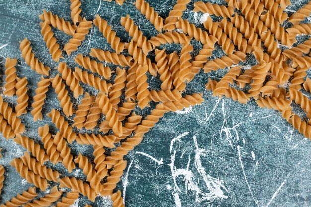 Braune rohe Fusilli-Nudeln auf blauem Raum verstreut.