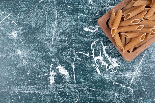 Braune rohe Penne-Nudeln auf Holzplatte.