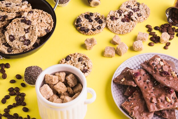 Brauner Zucker; Kekse; Kaffeebohnen und Schokoriegel auf gelbem Hintergrund