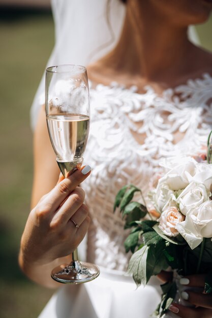 Braut hält Glas Champagner und einen Hochzeitsblumenstrauß draußen