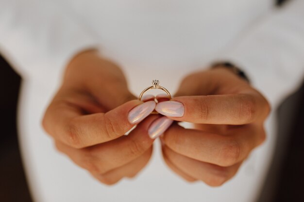 Braut hält Verlobungsring mit Diamant in Händen mit schöner Maniküre, Vorderansicht, Hochzeitstag