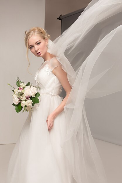 Braut im schönen Kleid steht drinnen im weißen Studio-Interieur wie zu Hause.