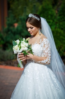Braut in einem weißen kleid mit einem blumenstrauß in den händen und einer krone auf dem kopf