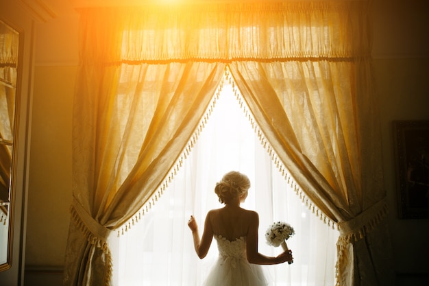 Braut mit Blumenstrauß neben dem Fenster
