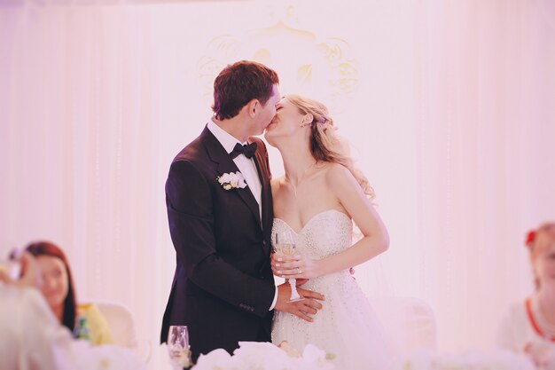 Braut mit einem Glas Champagner in der Hand küssen ihren Mann