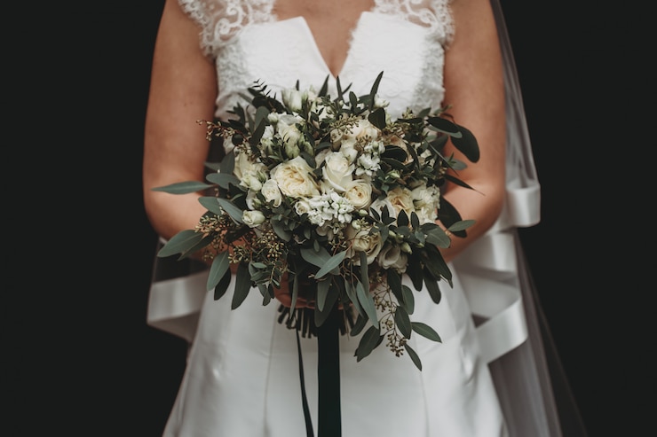 Kostenlose Foto braut mit einem weißen hochzeitskleid, das einen schönen blumenstrauß auf schwarz hält