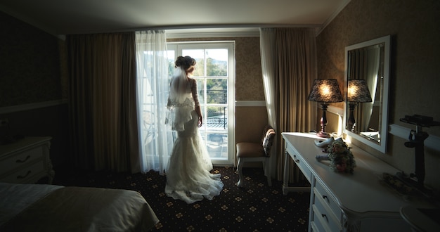 Braut schaut durch das Fenster vom Hotelzimmer