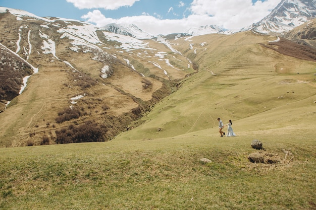 Braut und Bräutigam gehen auf das Gras im Sommer im Hochgebirge