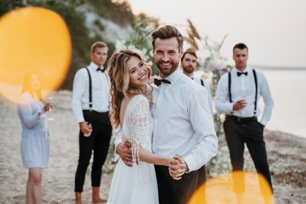 Braut und Bräutigam haben ihre Hochzeit mit Gästen am Strand