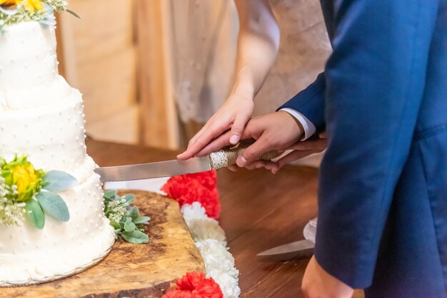 Braut und Bräutigam schneiden die schöne weiße Hochzeitstorte