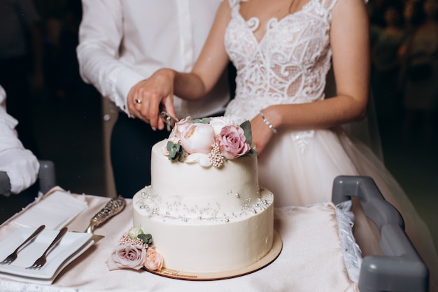 Braut und Bräutigam schneiden verziert mit Blumenhochzeitstorte