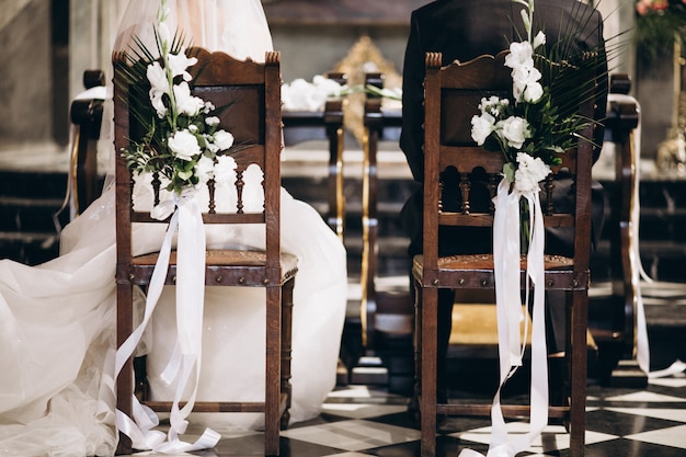 Braut und Bräutigam sitzen auf Stühlen an ihrem Hochzeitstag, von hinten