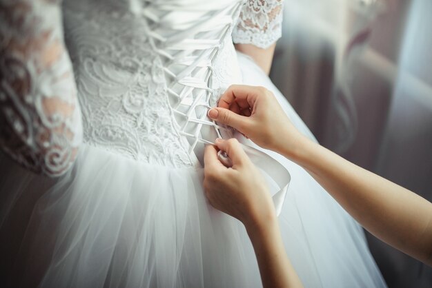 Brautjungfer macht Bogenknoten auf dem Rücken des Hochzeitskleides der Bräute