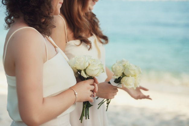 Kostenloses Foto brautjungfern mit weißen rosensträußen stehen am strand