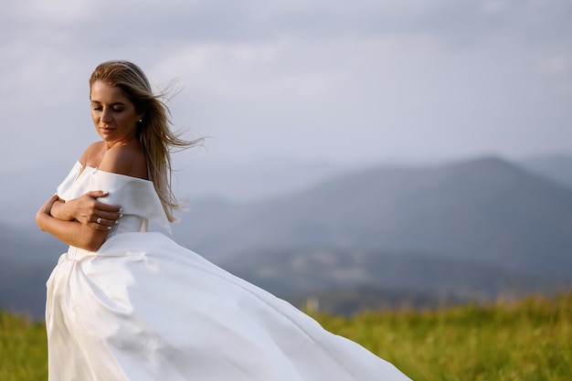 Brautmädchen im weißen Kleid, das auf Wiese mit Mauntains-Ansicht steht