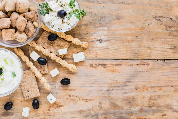 Breadsticks, Oliven, Knäckebrot und Gebäck mit Käseschüssel auf Holztisch