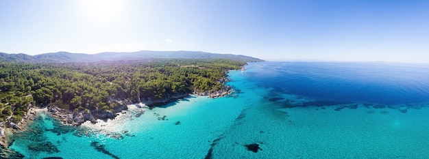 Breiter Schuss der ägäischen Seeküste mit blauem transparentem Wasser, Grün herum, Pamoramaansicht von der Drohne, Griechenland
