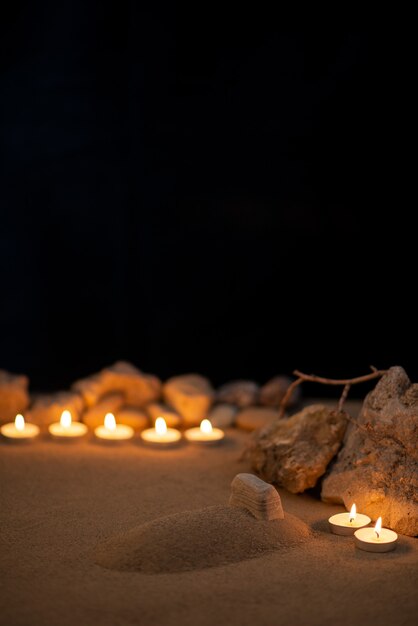 Brennende Kerzen um kleines Grab als Erinnerung auf dunkler Oberfläche