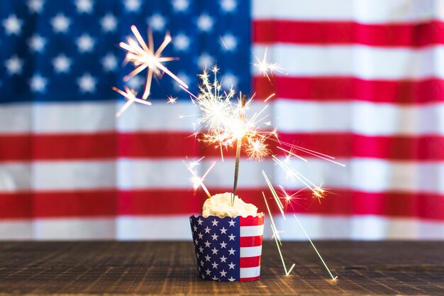 Brennende Wunderkerze auf kleinem Kuchen gegen defocused USA-Flaggenhintergrund