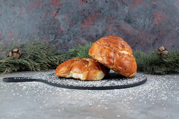 Brett mit zwei Brötchen neben Tannenzweigen auf Marmoroberfläche