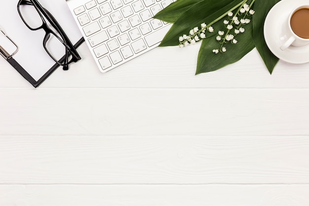 Brillen, Klemmbrett, Tastatur, Blume und Blätter mit Kaffeetasse auf Schreibtisch