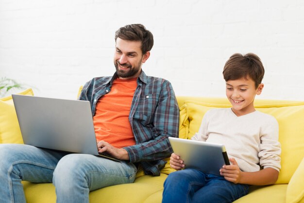 Bringen Sie das Arbeiten an dem Laptop und Sohn hervor, die auf Tablette schauen