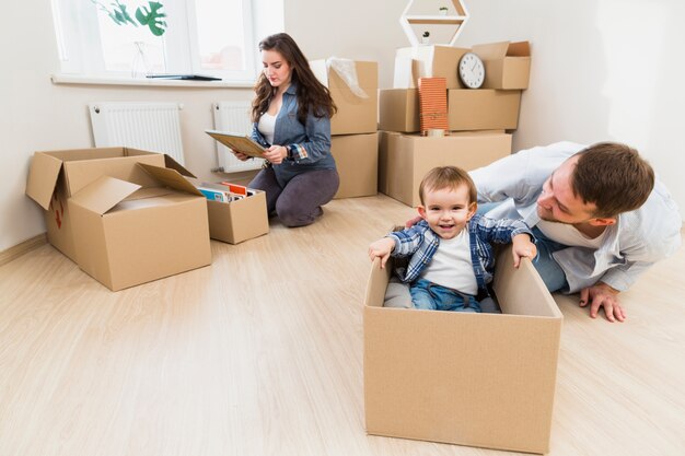 Bringen Sie das Spielen mit seinem Sohn und seiner Frau hervor, die die Pappschachtel am Hintergrund auspackt