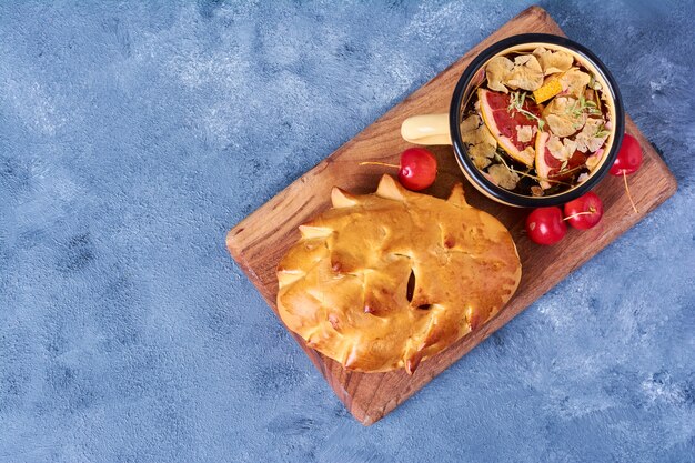 Brötchen mit Kräutergetränk auf einem Holzbrett auf Blau