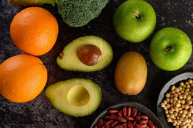 Brokkoli, Apfel, Orange, Kiwi, Hülsenfrüchte und Avocado auf einem schwarzen Zementboden.