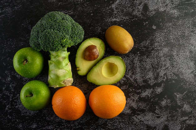 Brokkoli, Apfel, Orange, Kiwi und Avocado auf einem schwarzen Zementboden.