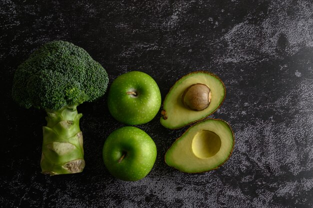 Brokkoli, Apfel und Avocado auf einem schwarzen Zementboden.