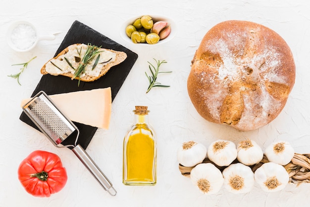 Brot mit Käse, Rosmarin, Öl, Tomate, Olive mit Bündel Knoblauchknollen O weißen Hintergrund