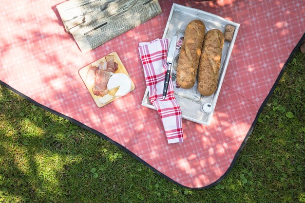 Brot; Speck und Käse auf rotem Tischtuch auf grünem Gras