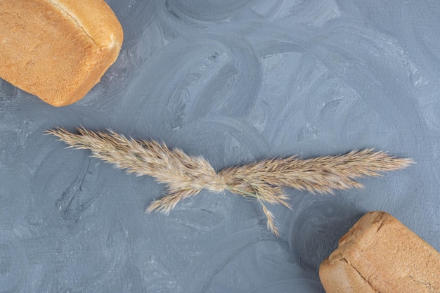 Kostenloses Foto brotklumpen mit federgrasstielen dazwischen auf marmorhintergrund.