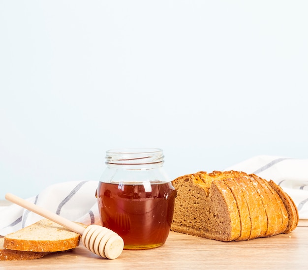 Brotscheibe und Glas Honig zum Frühstück über hölzernem Schreibtisch