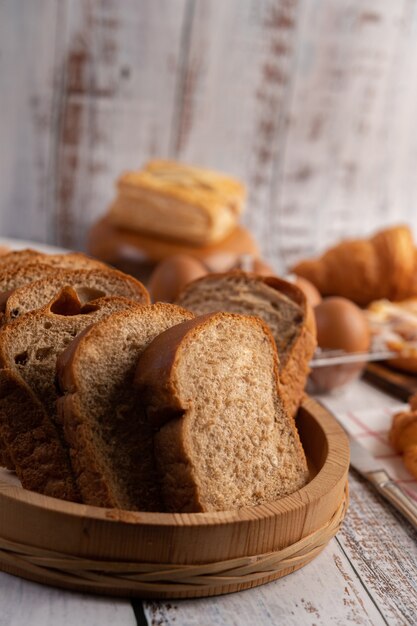 Brotscheiben in einem Holzteller auf einem weißen Holztisch platziert.