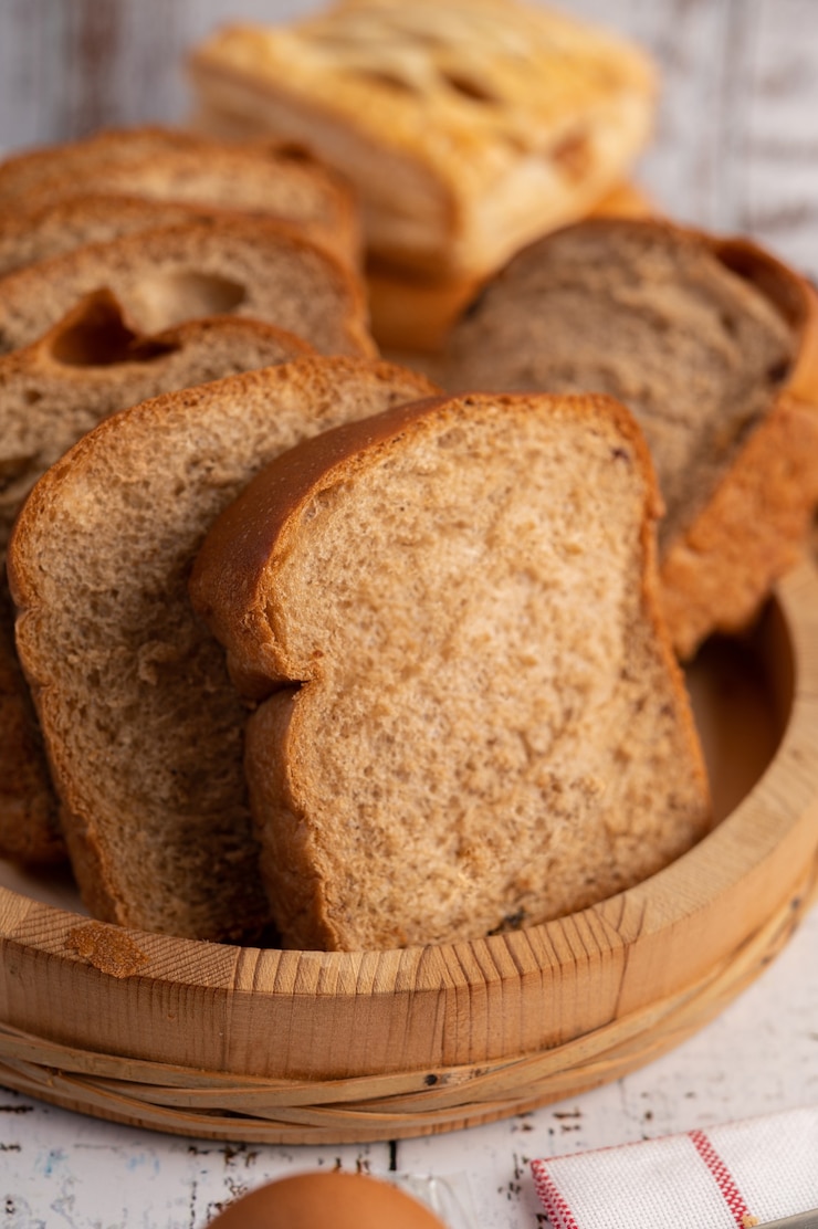 Kostenlose Foto brotscheiben in einem holzteller auf einem weißen holztisch platziert.