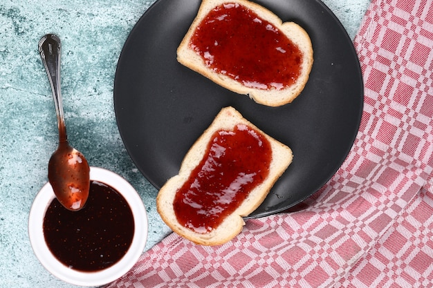 Brotscheiben mit Erdbeermarmelade in der grauen Platte und in einer Schale Marmelade.