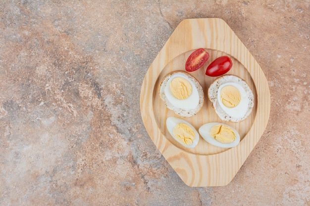 Brotscheiben mit gekochten Eiern und Tomaten auf Holzteller