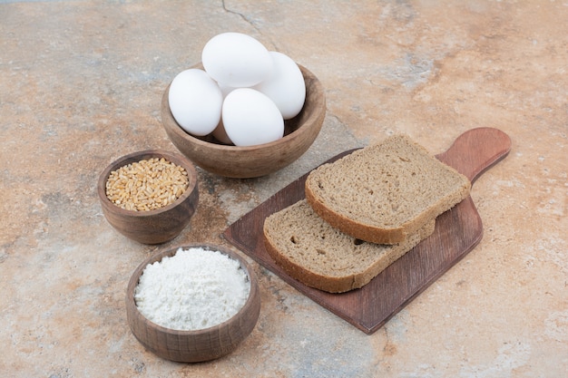 Brotscheiben, schalen mit eiern, mehl und gerste auf marmoroberfläche