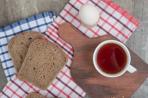 Brotscheiben und eine Tasse Tee auf Tischdecken mit Ei. Hochwertiges Foto