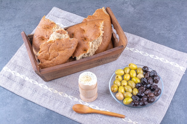 Brottablett, weich gekochtes Ei und eine Platte mit kernlosen Oliven auf einer kleinen Tischdecke auf Marmoroberfläche