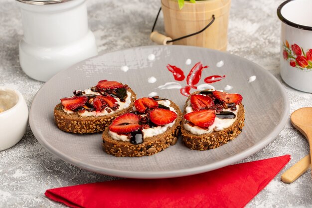 Brottoast aus der Nähe mit Erdbeeren und Sauerrahm in der Platte auf grau