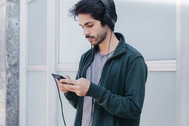 Browsing-Telefon des jungen Mannes mit Kopfhörern